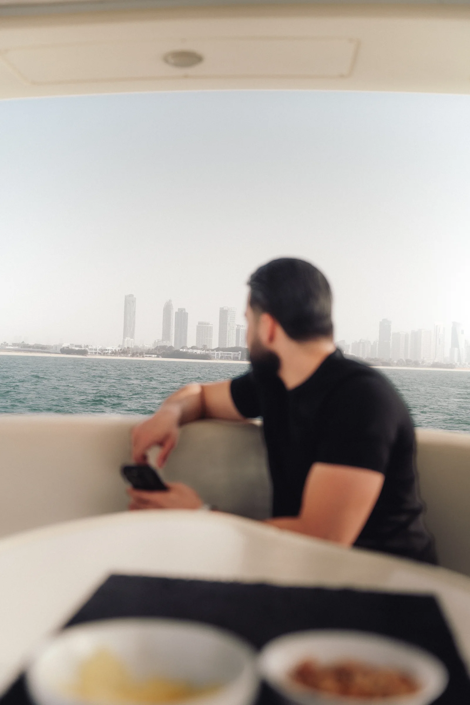 Zack Lalouti seated aboard a boat and looking across the water toward the Dubai skyline.