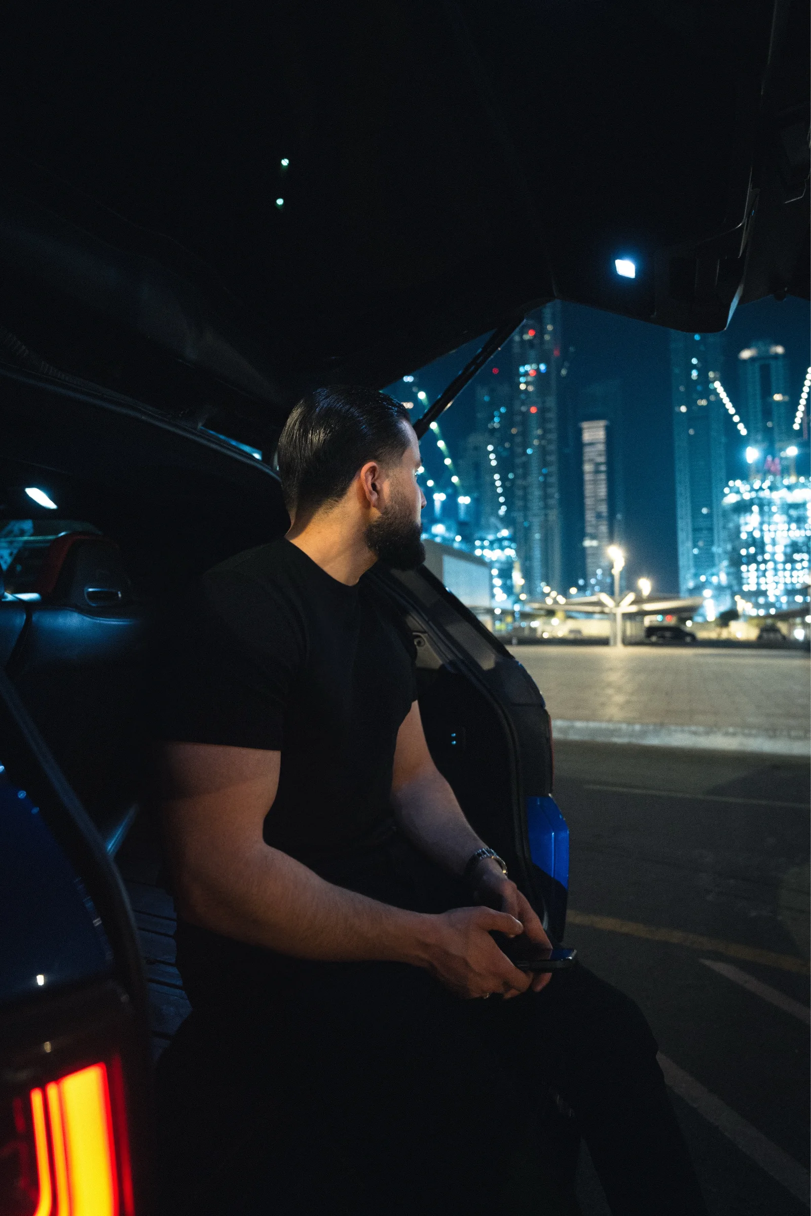 Zack Lalouti seated in an open car doorway with illuminated buildings behind him in Dubai at night.