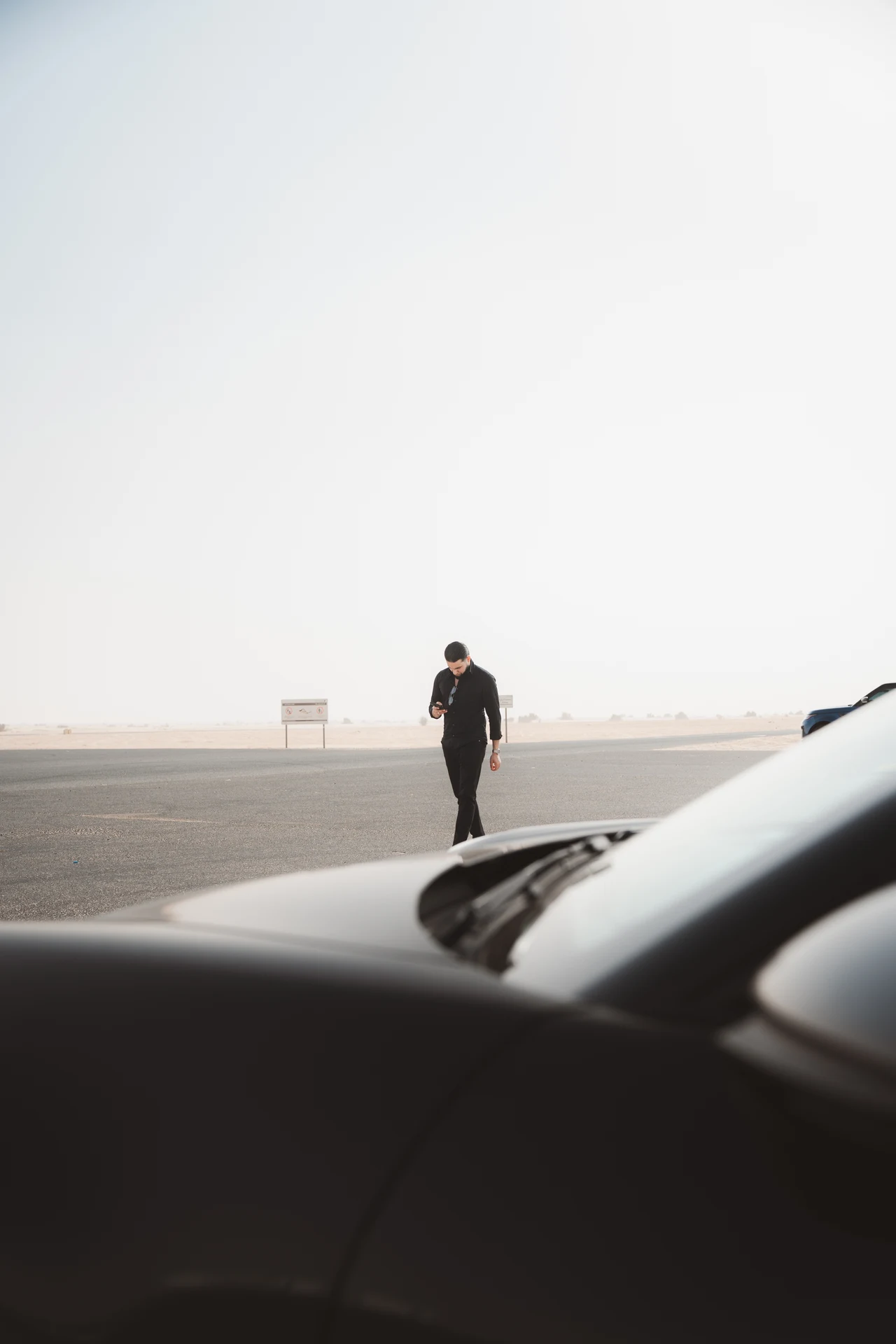 Zack Lalouti standing on a desert road in Dubai, viewed through a car window.