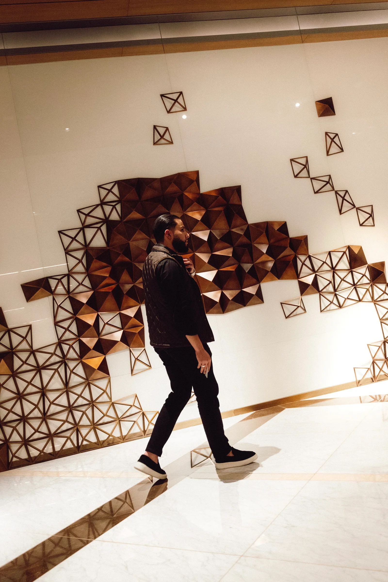 Zack Lalouti walking past a geometric wall installation in a bright interior in Dubai.