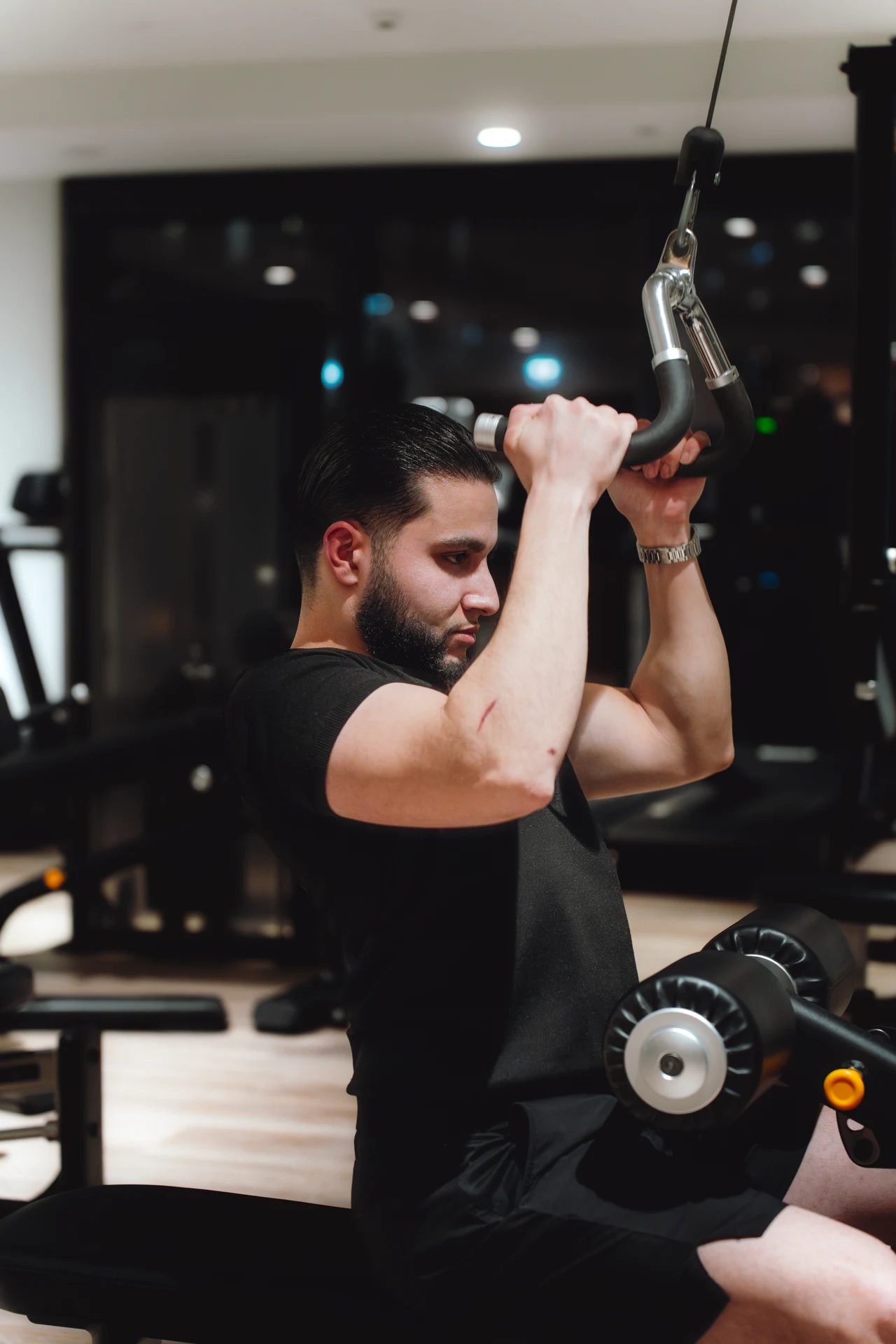 Zack Lalouti holding a cable attachment overhead while seated at a gym in Dubai.