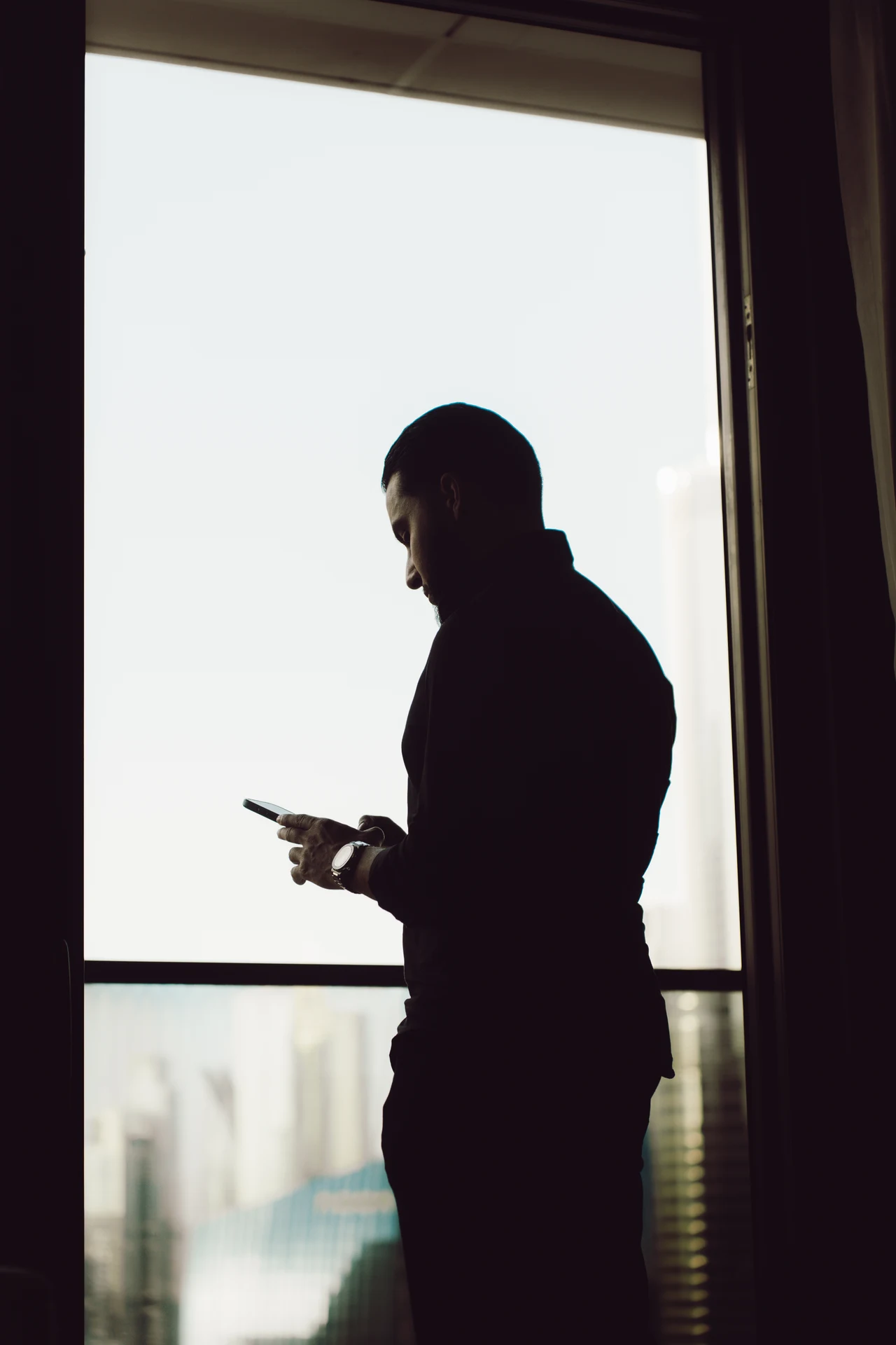 Silhouette of Zack Lalouti looking at his phone beside a large window in Dubai.
