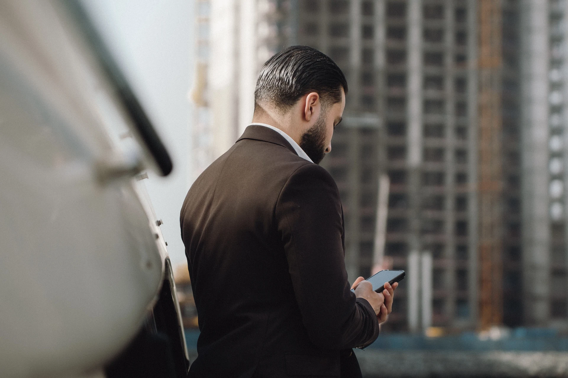 Zack Lalouti standing on a yacht and using his smartphone, with waterfront buildings behind him.