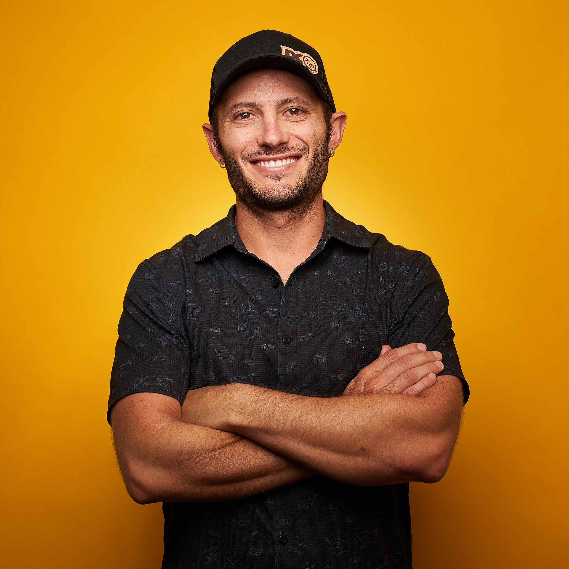 This is a picture of the Austin, Texas-based entrepreneur Noah Kagan. He's standing in front of an orange background with his arms crossed.