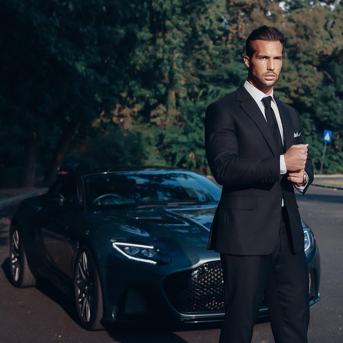 Tristan Tate in a black suit beside a car.