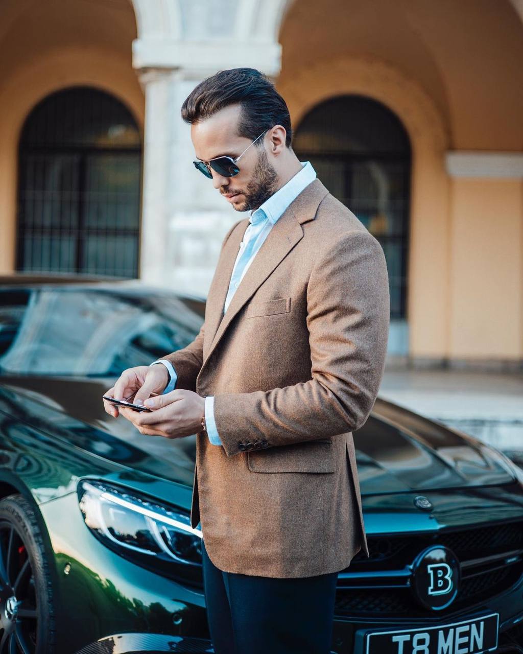 Tristan Tate standing beside a car in a brown jacket.